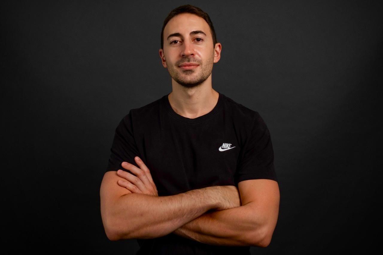 Man in black Nike t-shirt with arms crossed against dark background.