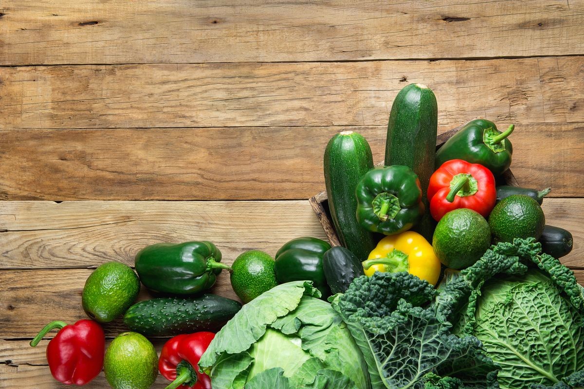 Variety Fresh Organic Green Vegetables Savoy Cabbage Zucchini Cucumbers Red Yellow Bell Peppers Avocados on Weathered Plank Barn Wood Background. Superfoods Vegan Plant Based Diet Concept. Copy Space